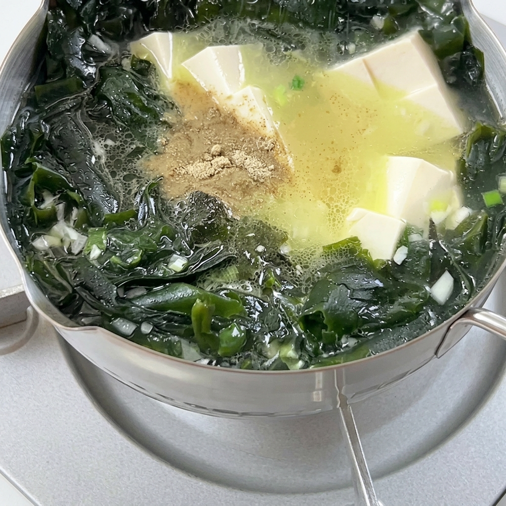 Poivre en poudre saupoudré dans une marmite de soupe bouillonnante contenant des algues wakame et des cubes de tofu.