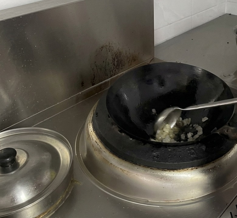 Un cuisinier remue des cristaux de sucre en train de fondre dans un wok à laide dune grande louche en métal.