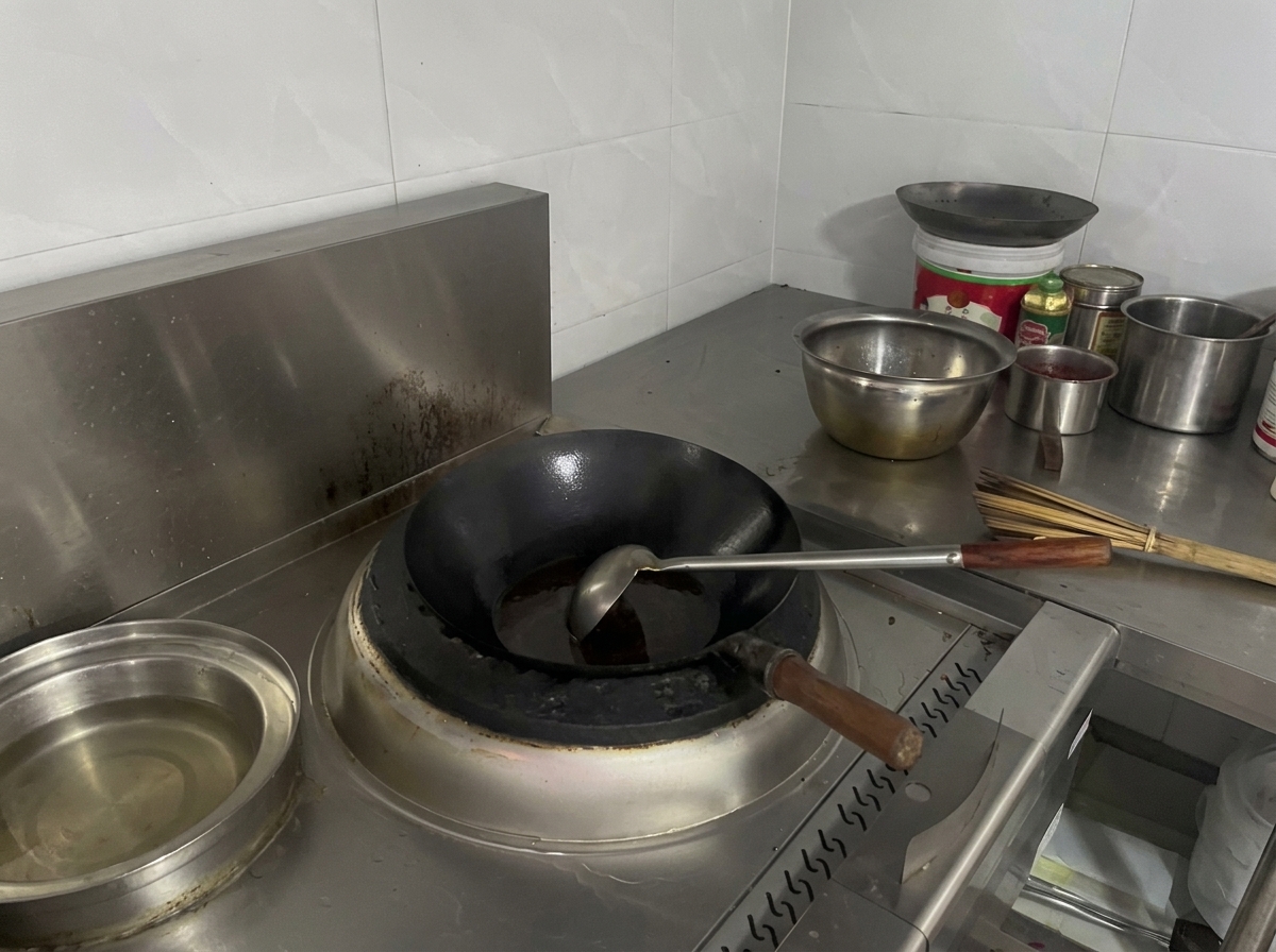 Un wok posé sur la gazinière, rempli dun liquide frémissant de couleur brun rougeâtre foncé.