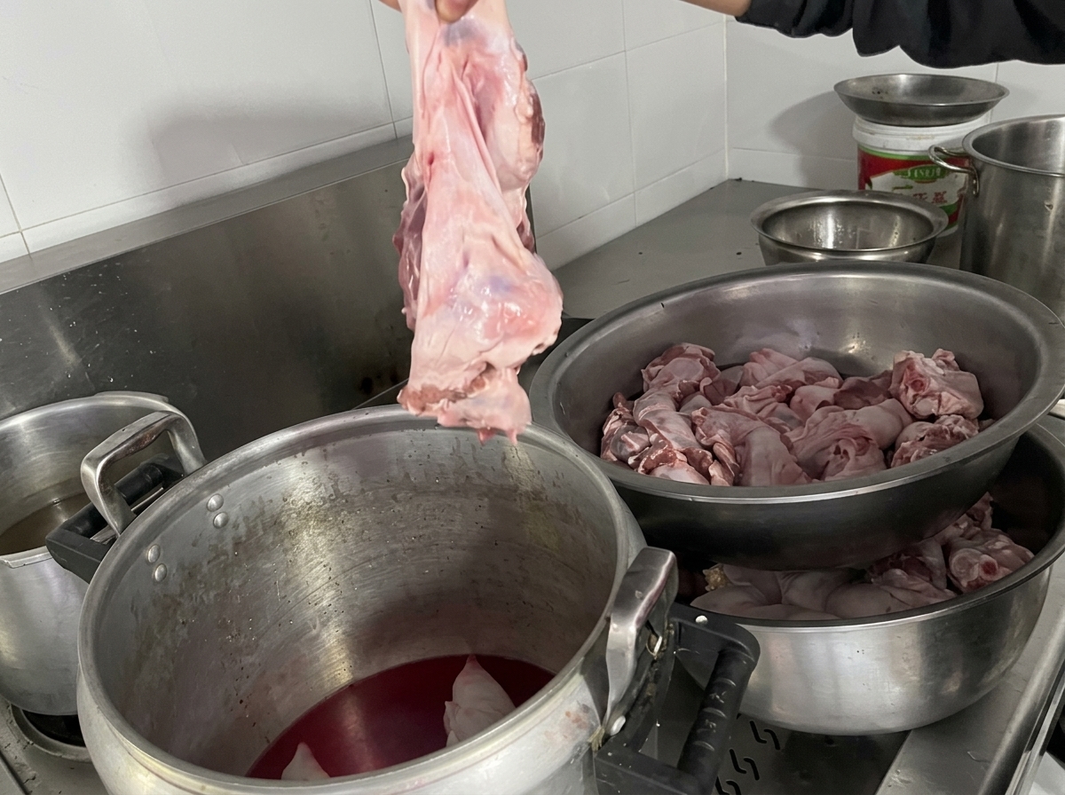 Une main tient un large morceau de hampe de bœuf crue, prête à le plonger dans la marmite contenant le bouillon et le porc.