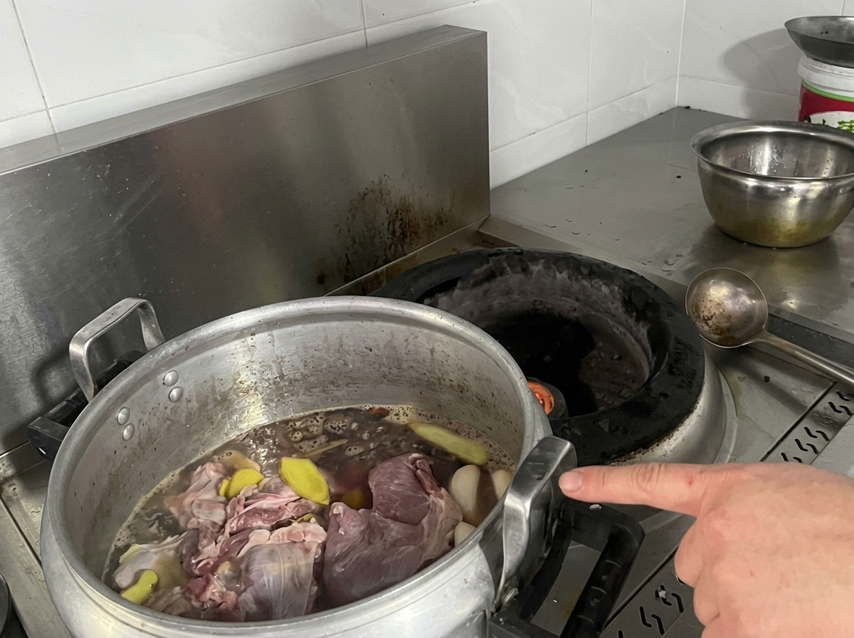 Une immense marmite en aluminium remplie de morceaux de viande, de tranches de gingembre et de bouillon foncé sur le feu.