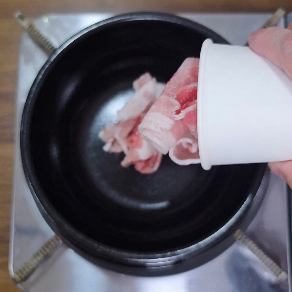 Main versant des tranches de poitrine de porc dans une marmite noire.