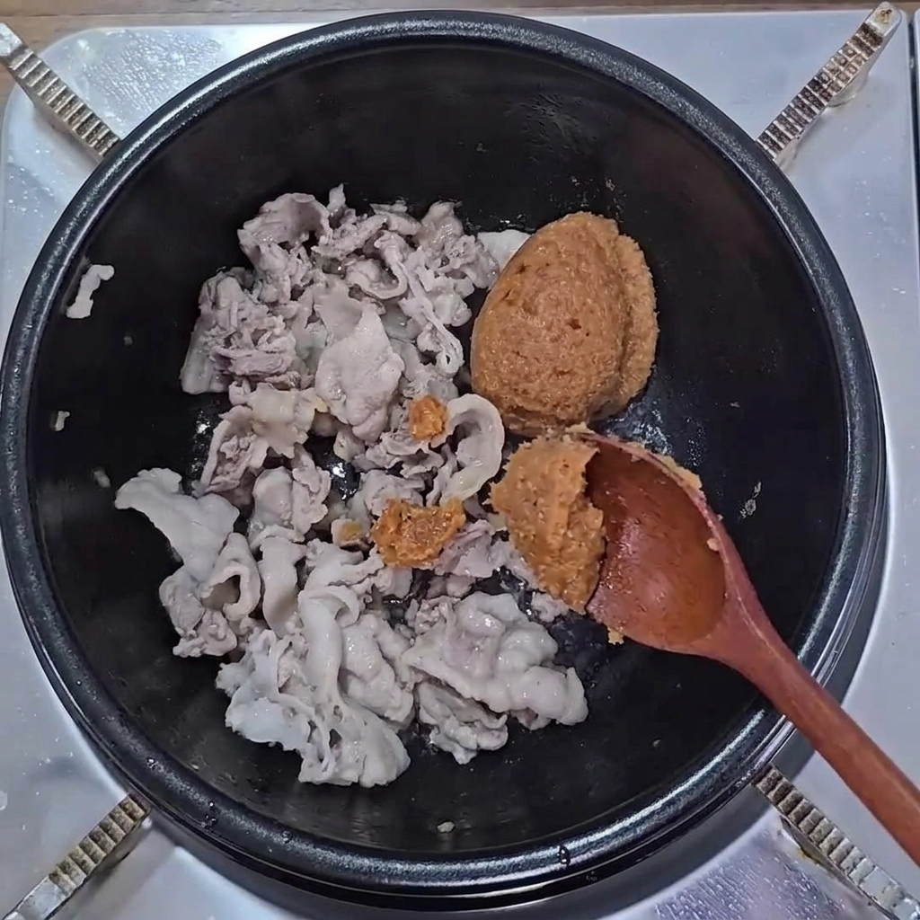 Cuillères de pâte de soja et de ssamjang ajoutées sur le porc cuit.