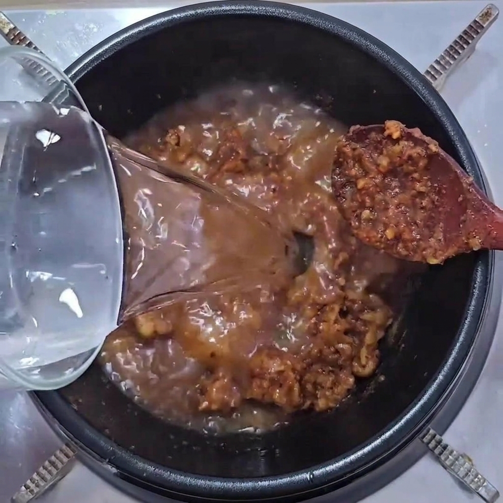 Eau versée dans la marmite contenant le mélange de porc et de pâtes.