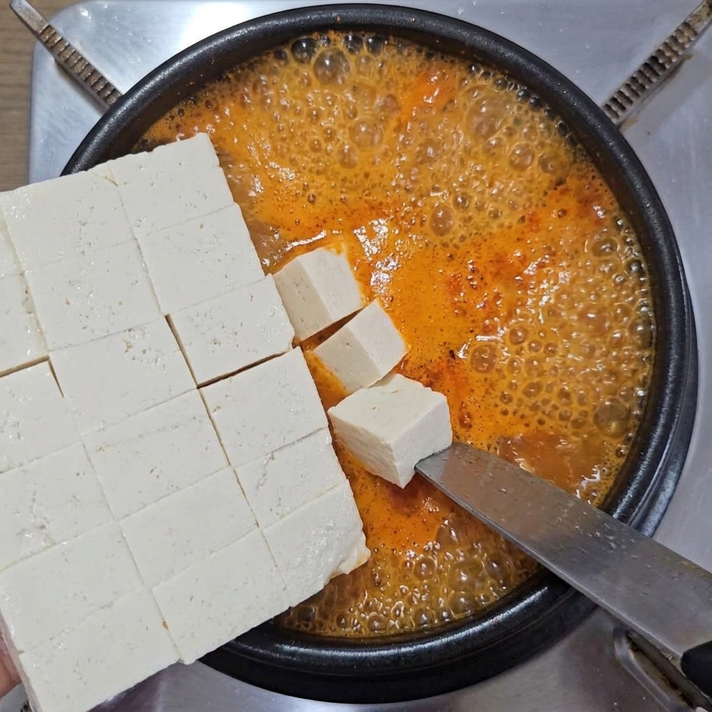 Tofu en dés glissé dans le centre du ragoût bouillonnant.