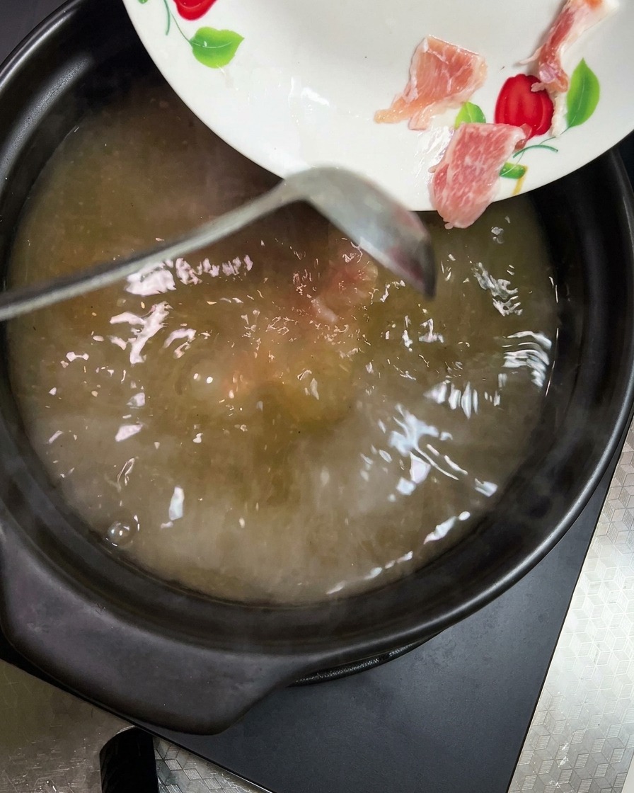 Morceaux de carotte orange et de pomme de terre jaune pâle ajoutés dans la soupe mijotante.