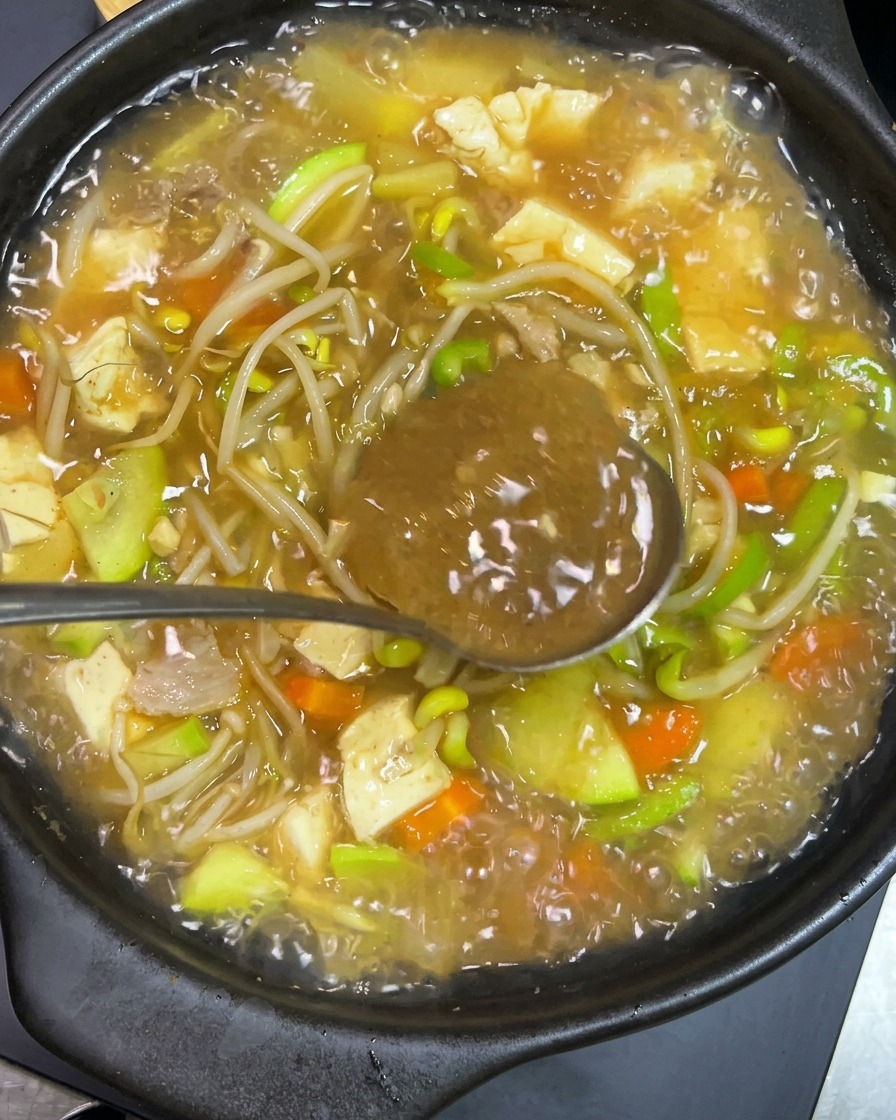 Une cuillère métallique tenant de la pâte pimentée coréenne sombre mélangée dans un bouillon bouillonnant.