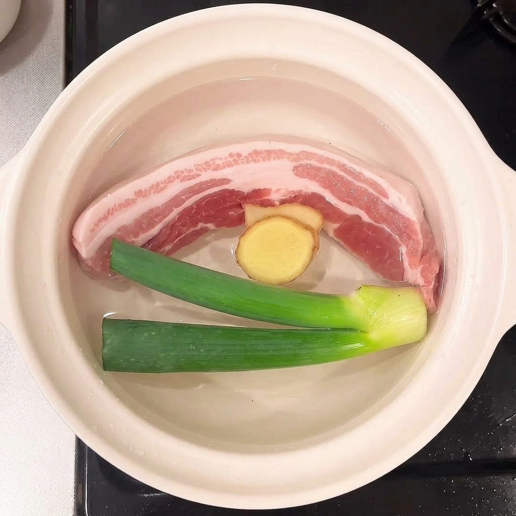 Des cébettes et des tranches de gingembre flottant dans leau avec le porc.
