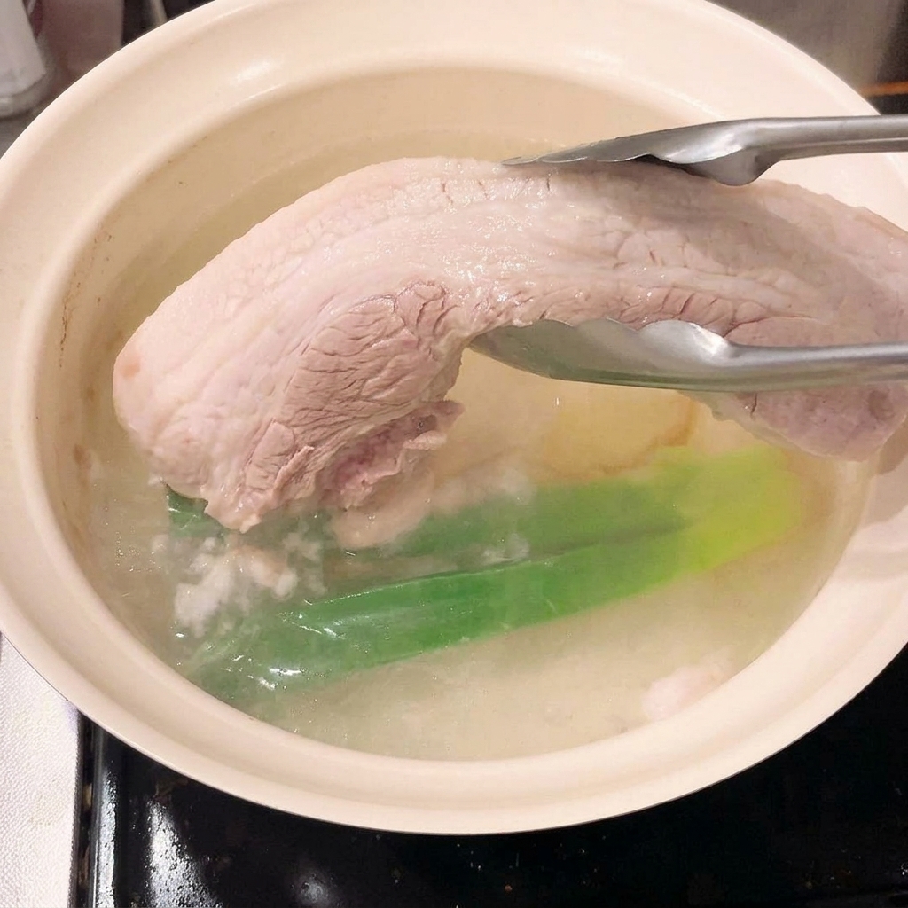 Une pince sortant le morceau de poitrine de porc ferme et blanchi de leau bouillante.