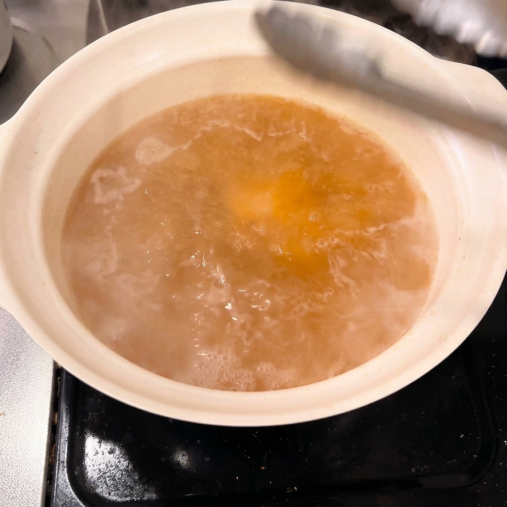 Des morceaux épais de poitrine de porc préalablement coupés et placés délicatement dans une marmite de bouillon au miso avec des pinces.
