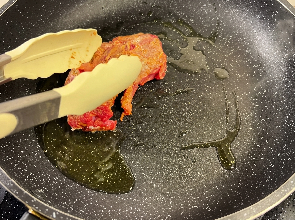 Une pièce de bœuf assaisonnée saisie dans une poêle chaude avec de lhuile, maintenue avec une pince.