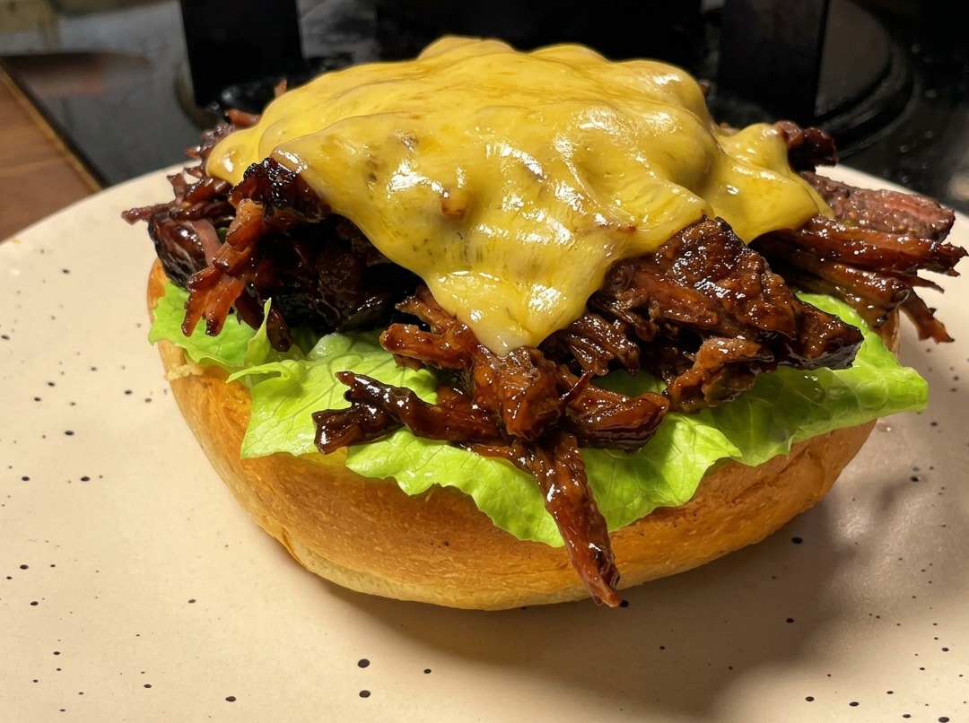 Un burger à leffiloché de bœuf recouvert dune tranche de fromage fondue à laide dun chalumeau de cuisine.