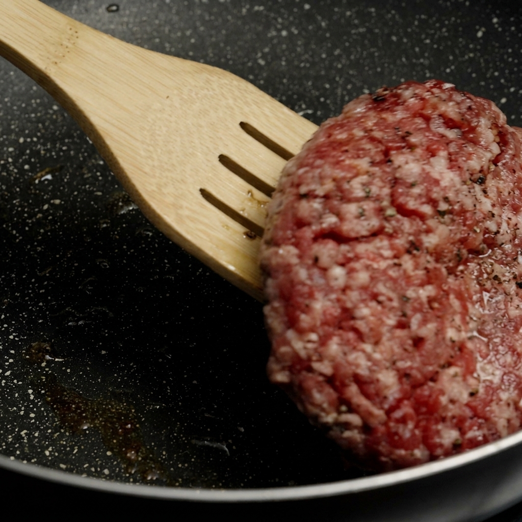 Une spatule en bois soulevant et retournant un steak épais présentant une belle croûte dorée dans une poêle chaude.