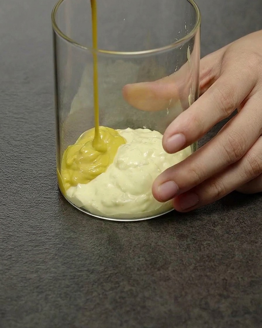 Une sauce burger onctueuse jaune pâle remuée dans un récipient en verre transparent.