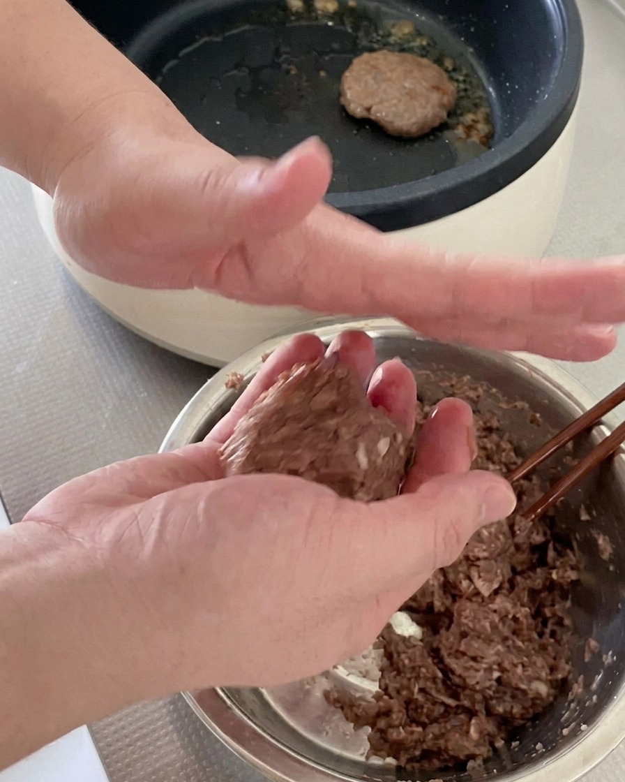 Deux mains malaxant et façonnant une portion de bœuf haché cru pour en faire un steak de burger rond.