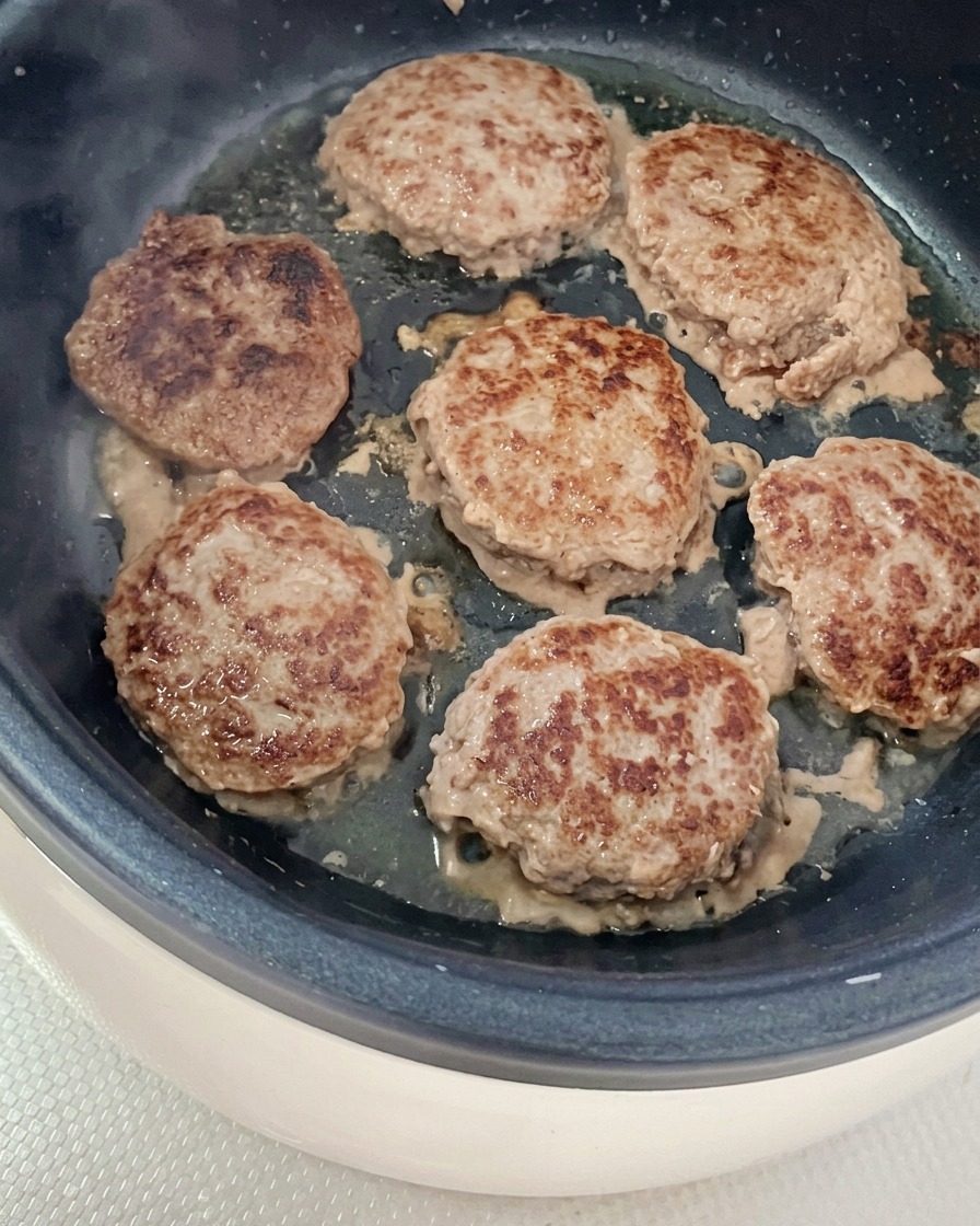 Plusieurs steaks hachés ronds en train de dorer dans une poêle légèrement huilée.
