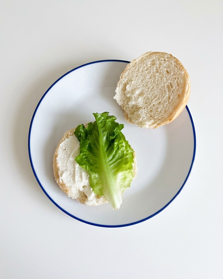 De la laitue verte bien fraîche déposée sur la base dun pain à burger recouverte de sauce.