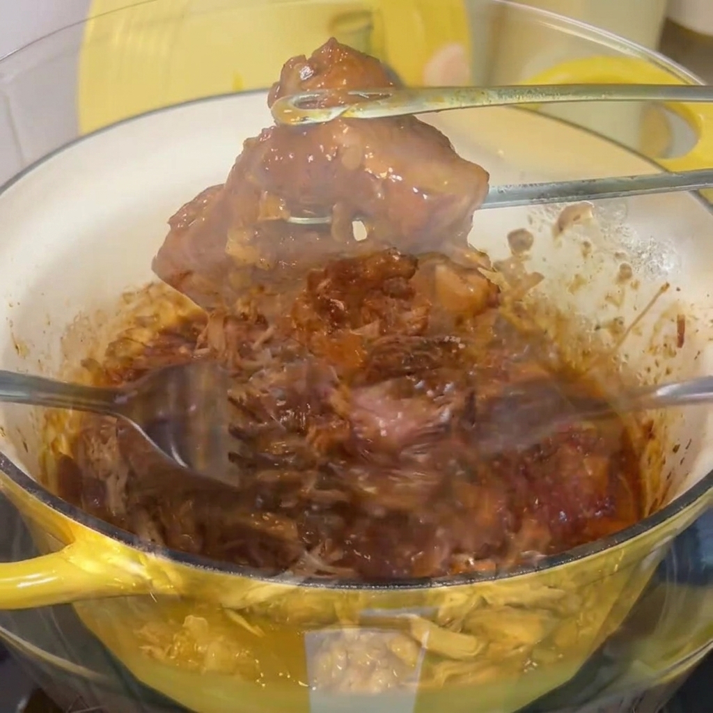 Porc braisé effiloché avec deux fourchettes dans un grand bol en verre.