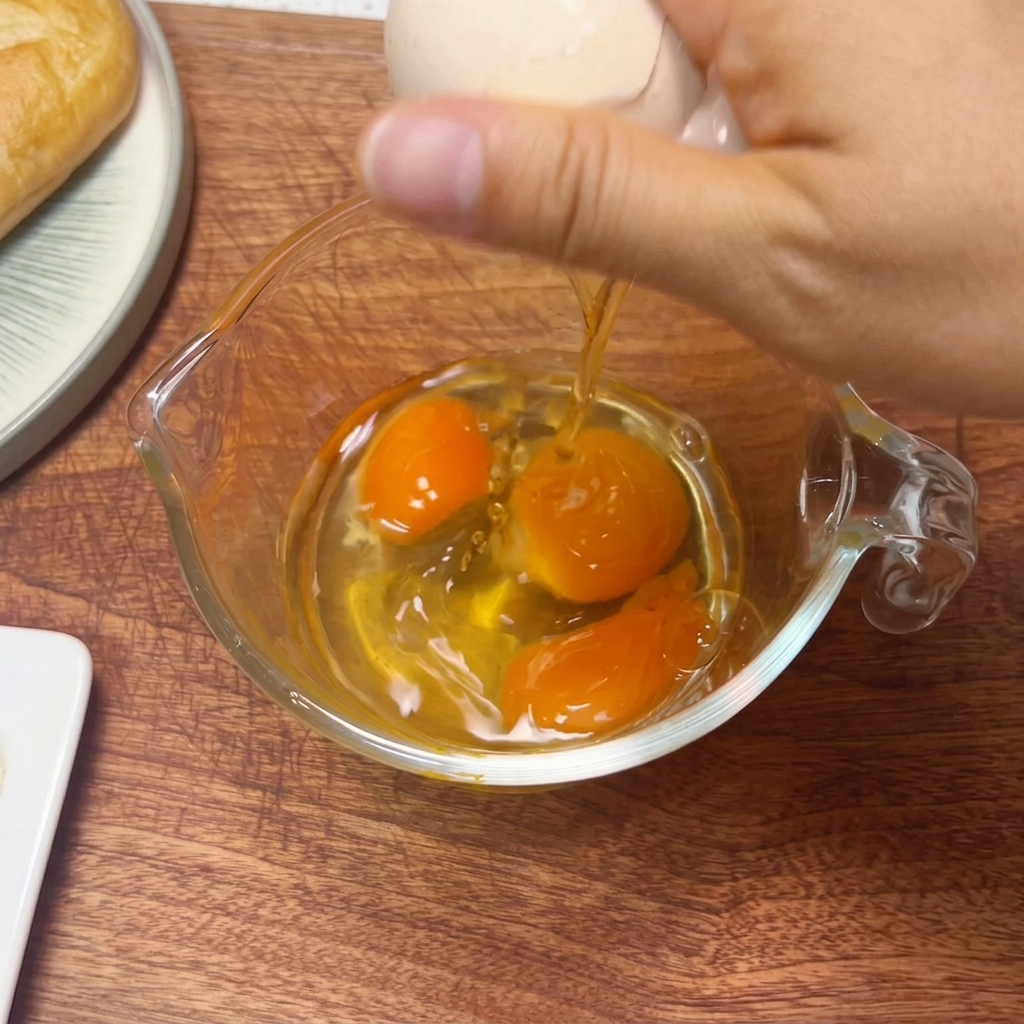 Trois œufs crus battus avec des baguettes dans un verre doseur.