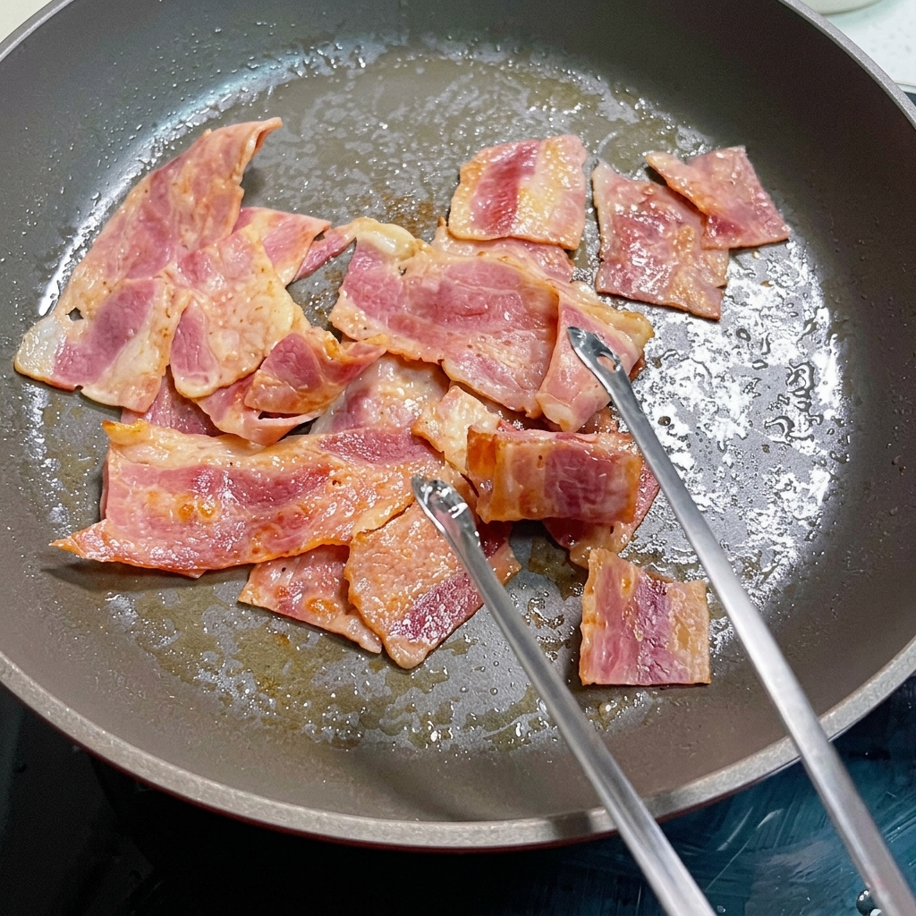 Œufs en train de cuire avec les morceaux de bacon dans la poêle.