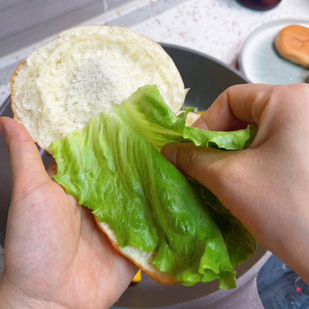 Assemblage du burger avec la laitue fraîche, le bacon et les œufs sur le pain.