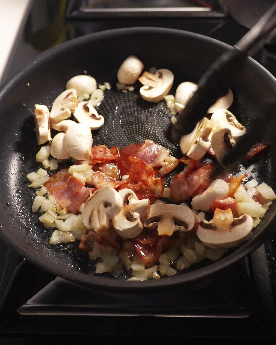 Champignons de Paris émincés revenus à la poêle avec les lardons, les oignons et lail.