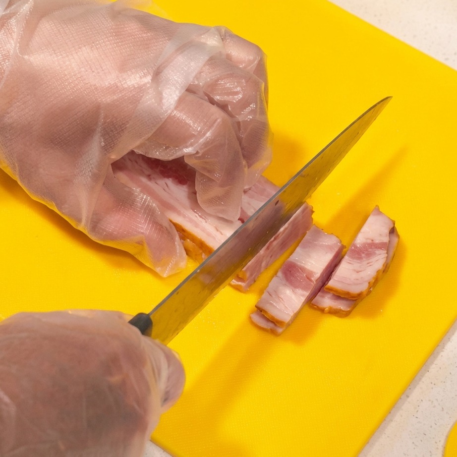 Tranches épaisses de bacon cru coupées en lanières sur une planche à découper jaune vif.