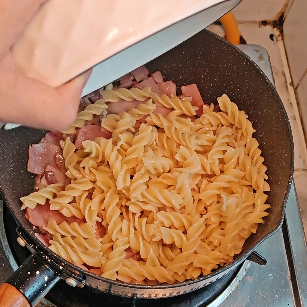 Fusillis cuits et tronçons dasperges ajoutés dans la poêle avec le bacon et les oignons.