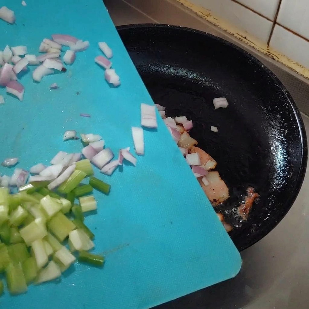 Aromates hachés ajoutés dans la poêle avec le bacon en train de frire.