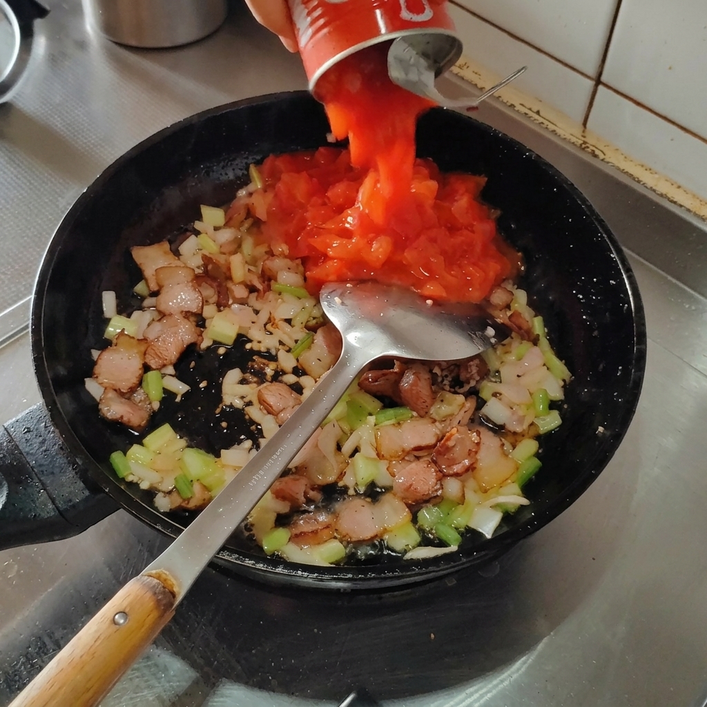 Tomates en conserve versées dans la poêle sur le mélange de bacon et daromates.