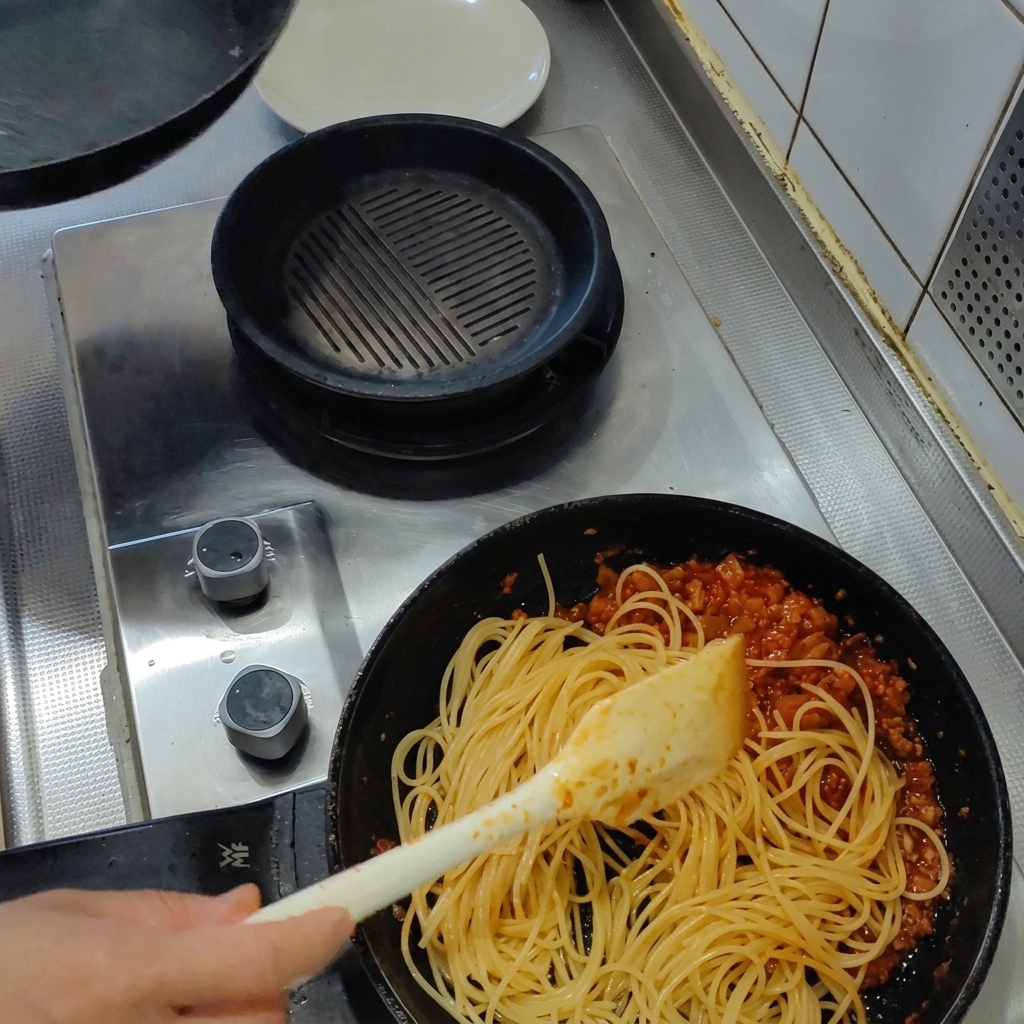 Spaghettis cuits mélangés avec une spatule dans la poêle de sauce tomate au bacon.