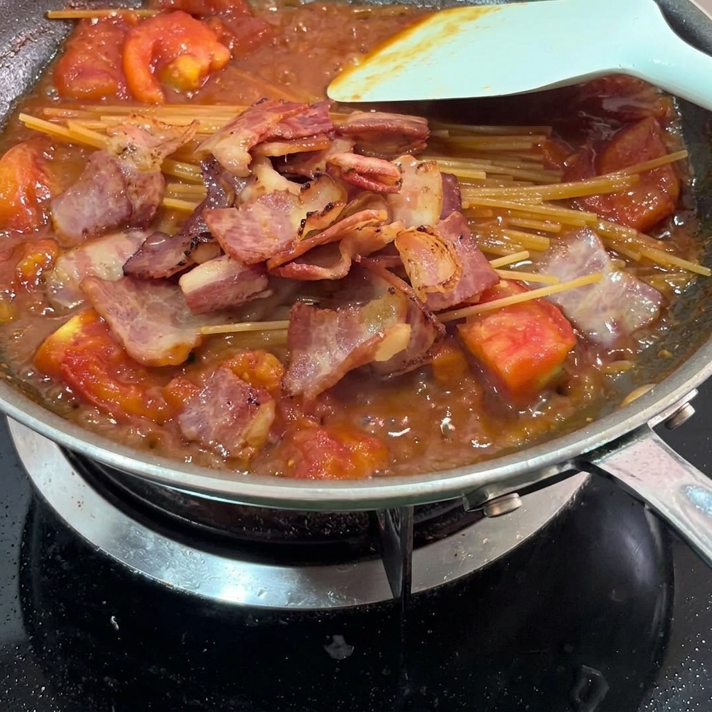 Morceaux de bacon frit mélangés aux pâtes et à la sauce.