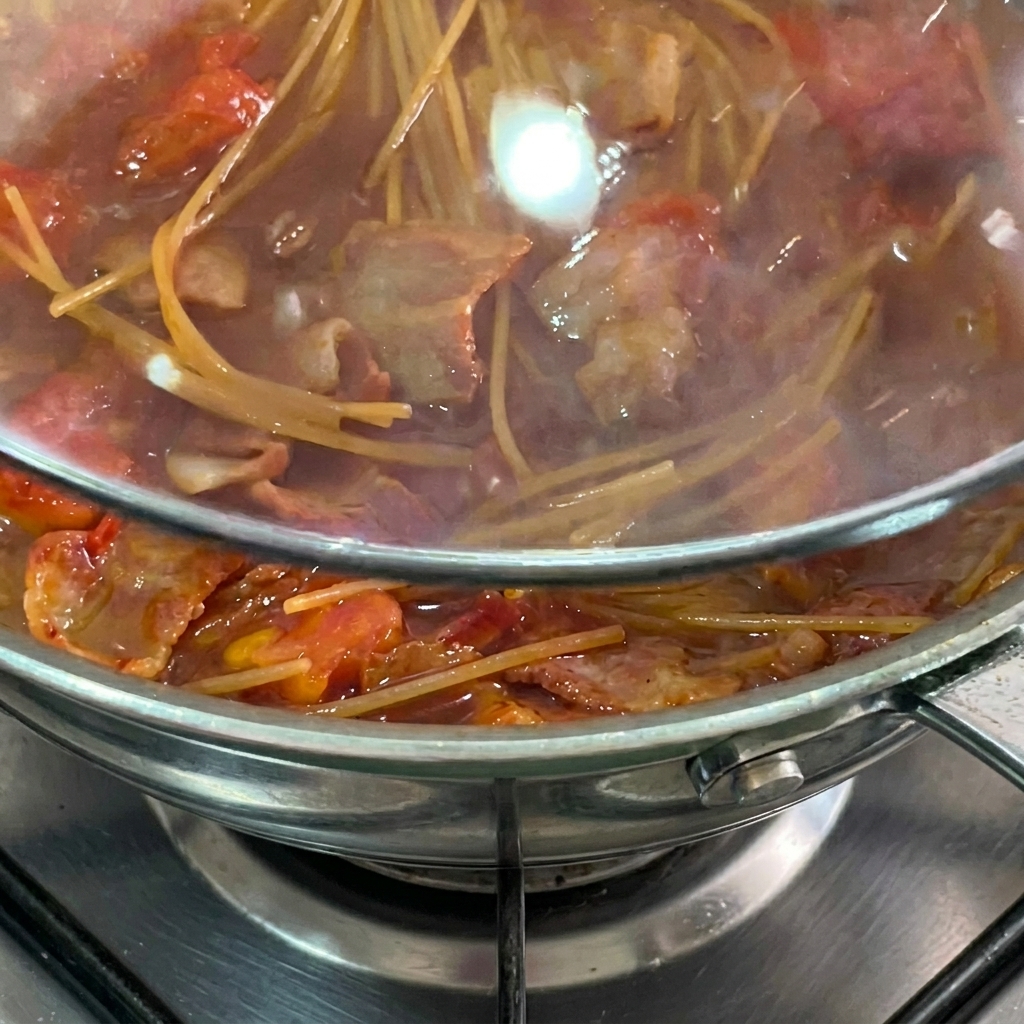 Spaghettis qui mijotent dans la poêle sous un couvercle.