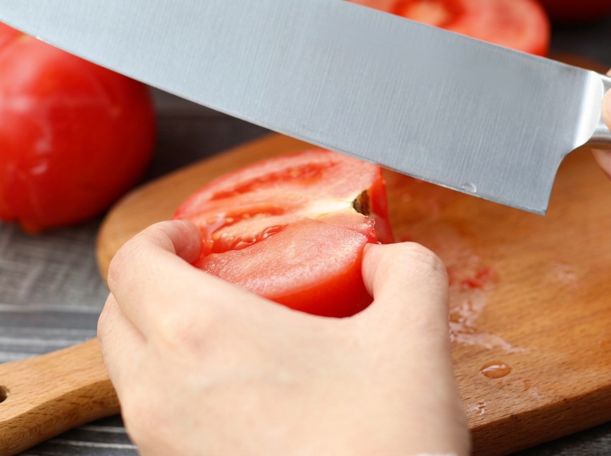 Couteau tranchant une tomate pelée sur une planche à découper en bois.