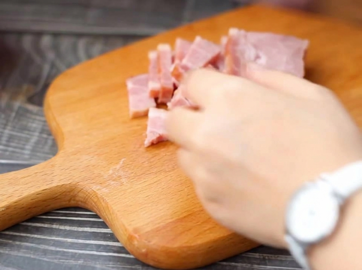 Tranches de bacon coupées en lamelles sur une planche à découper.