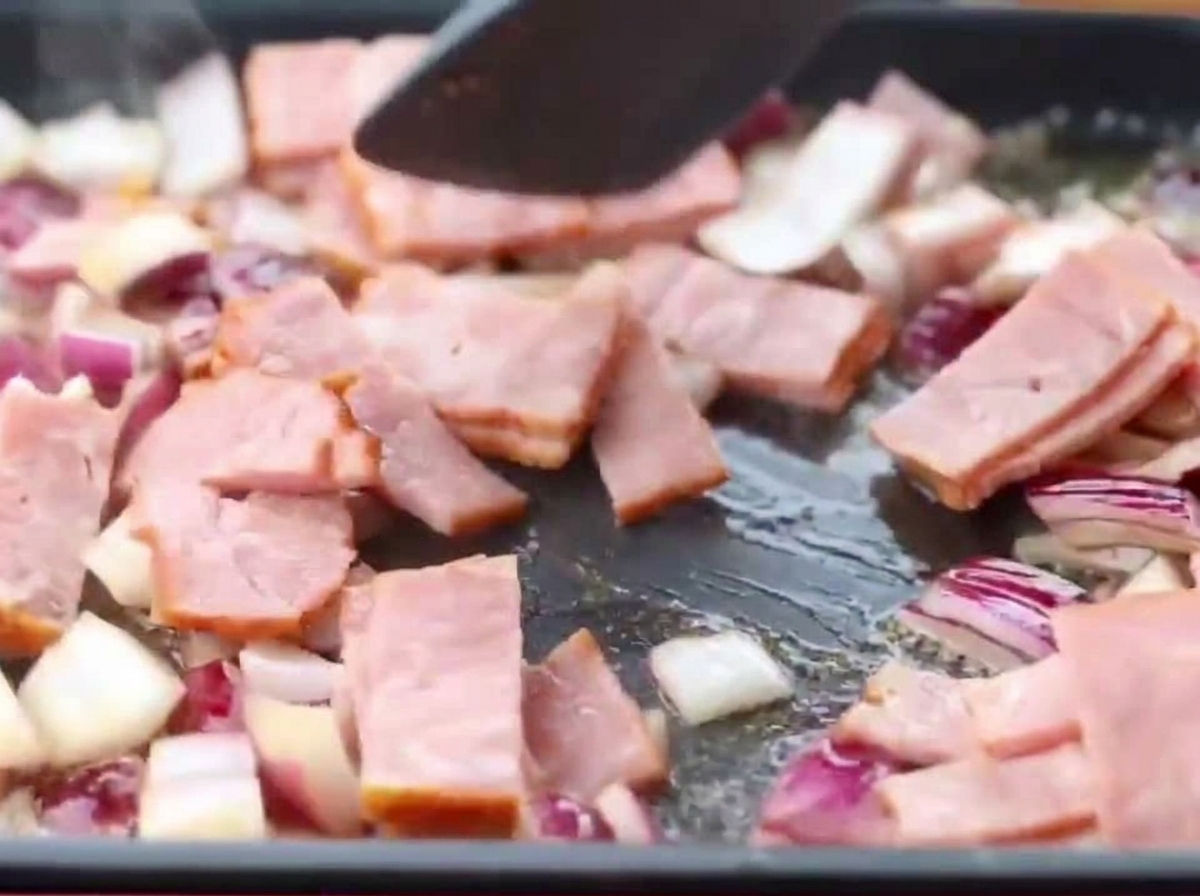 Lardons et oignons revenant ensemble dans une poêle.