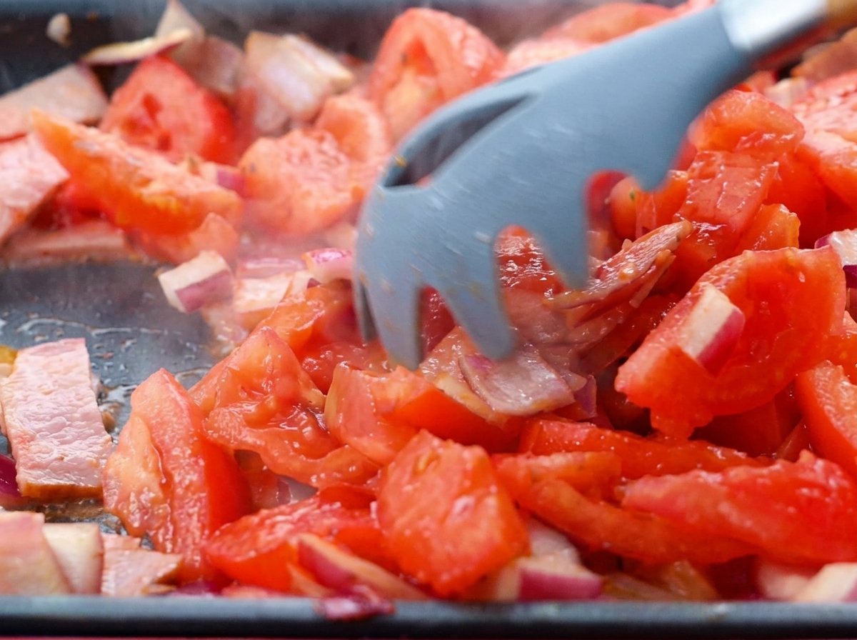 Tomates en dés mélangées au bacon et aux oignons dans la poêle.