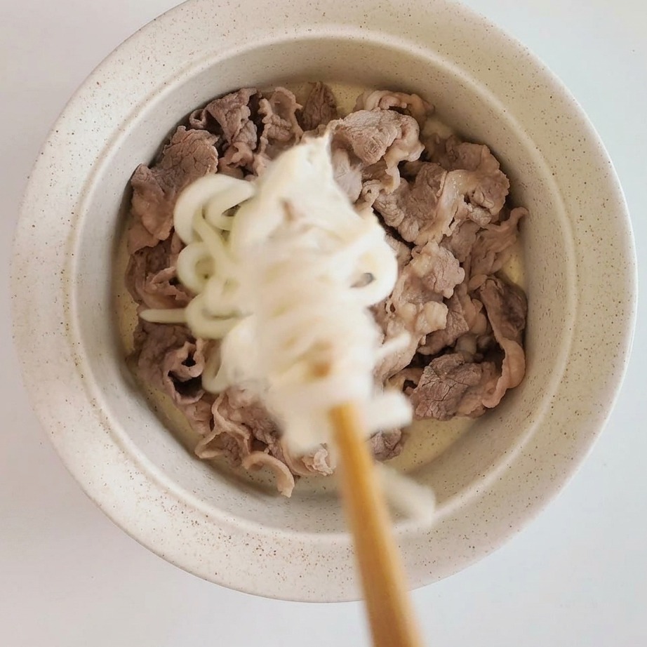 Bol assemblé avec des tranches de bœuf tendre surmontées dudon et de champignons enoki.
