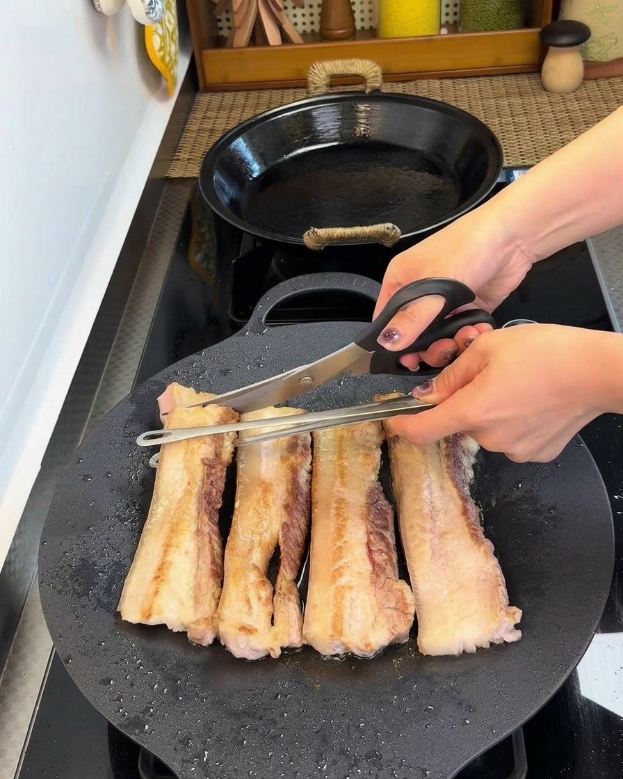 Ciseaux de cuisine coupant des tranches de porc dorées en petits morceaux directement dans la poêle.