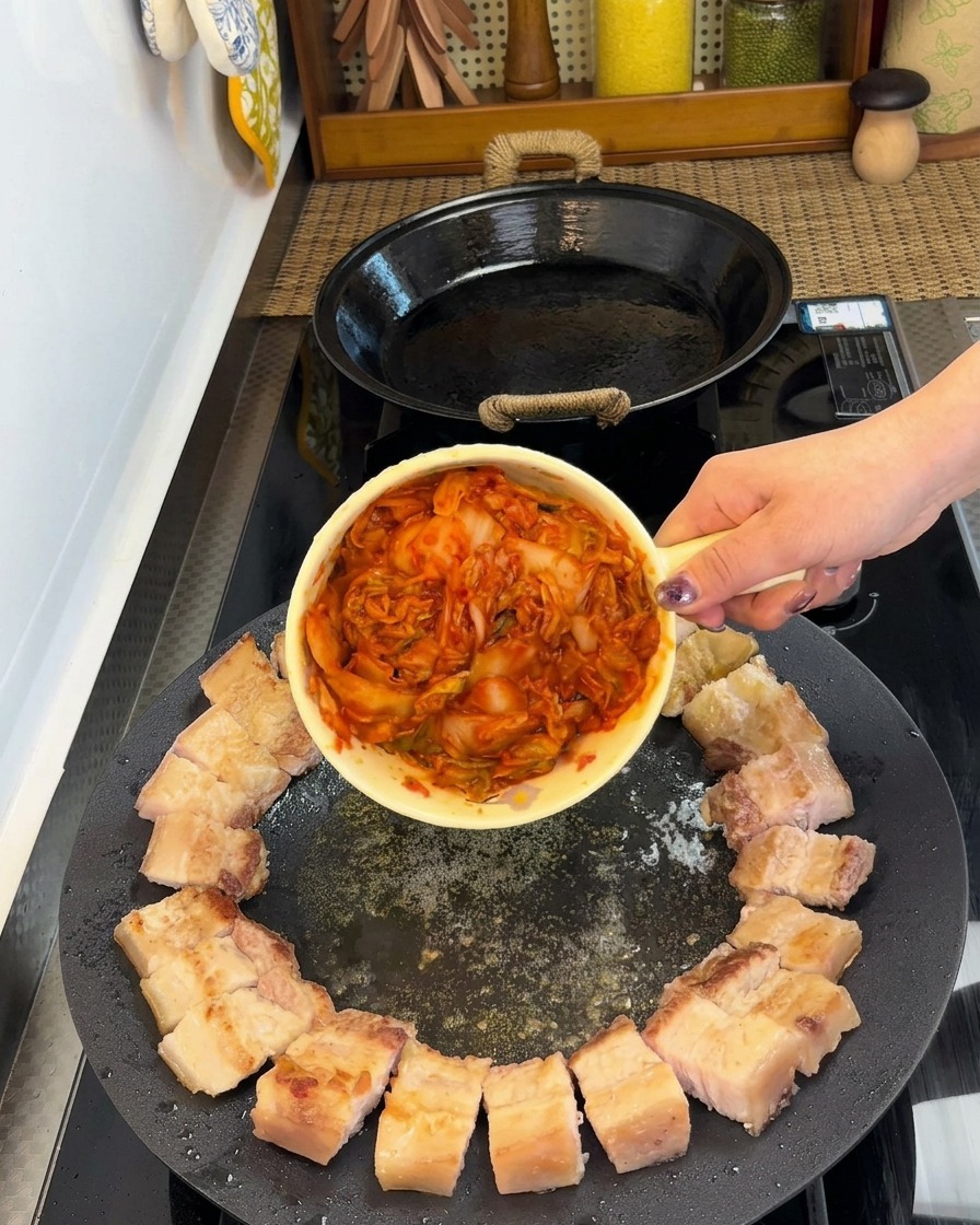 Morceaux de porc disposés en cercle avec le kimchi au centre de la poêle.
