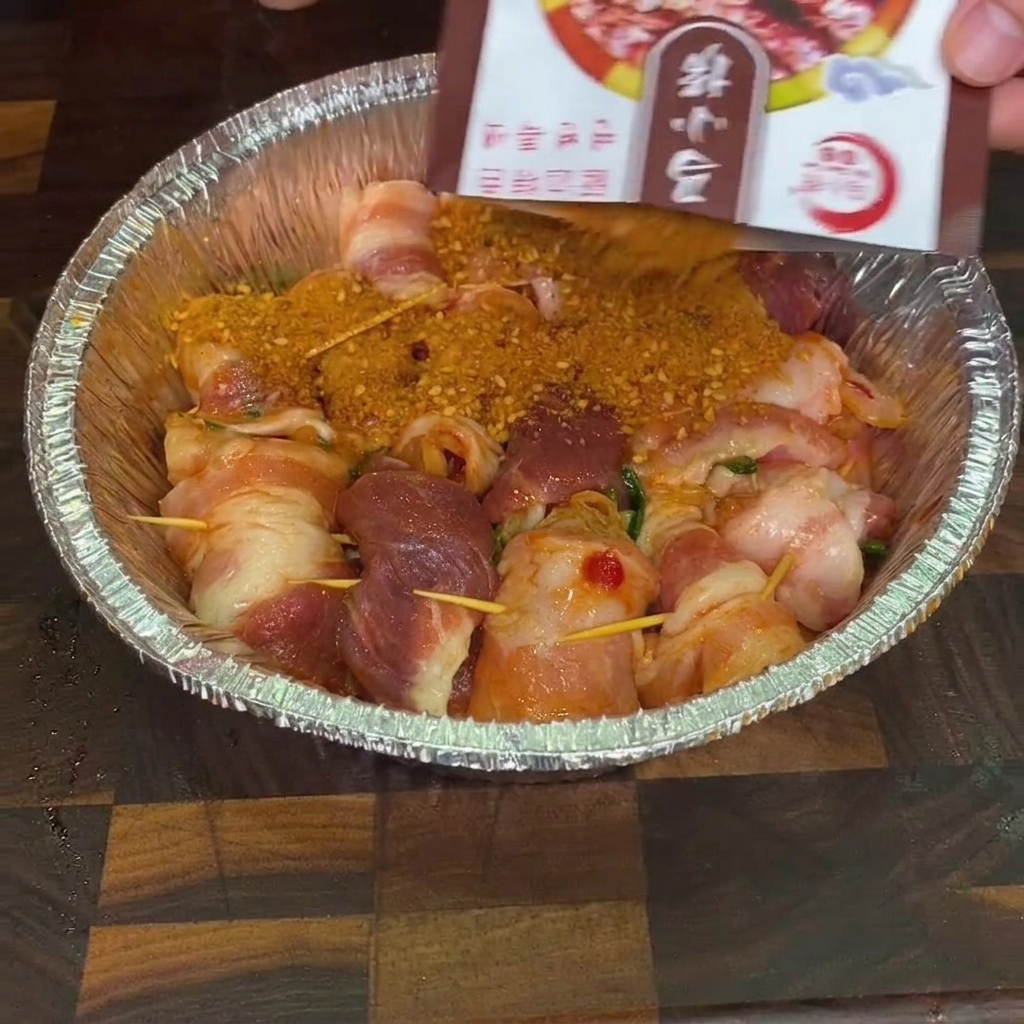 Mélange dépices barbecue saupoudré sur des roulés de porc crus dans un plat en aluminium.