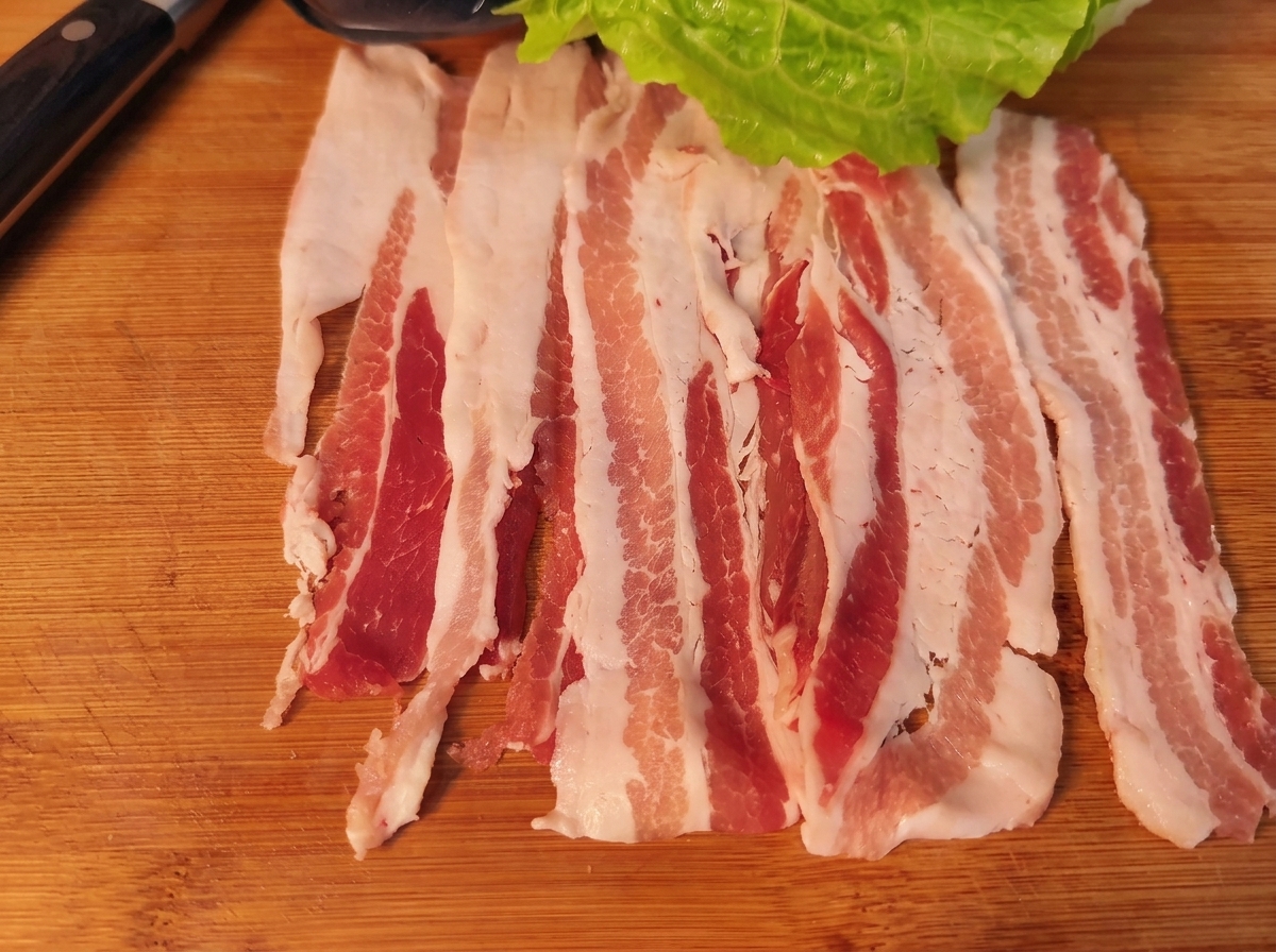 Une tranche de poitrine de porc garnie dune feuille de laitue, de carotte, doignon et de kimchi, prête à être roulée.