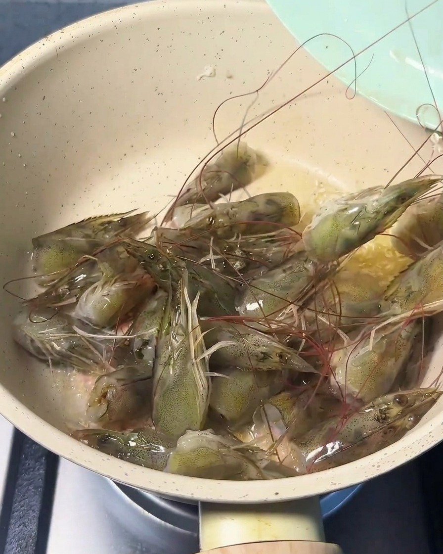 Têtes de crevettes fraîches crépitant dans une poêle avec de lhuile, devenant roses.