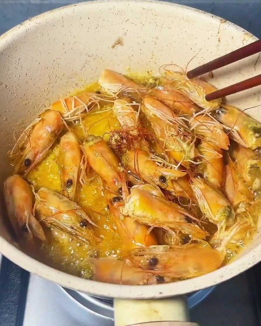Gros plan sur des têtes de crevettes pressées avec une spatule, libérant une huile orangée.