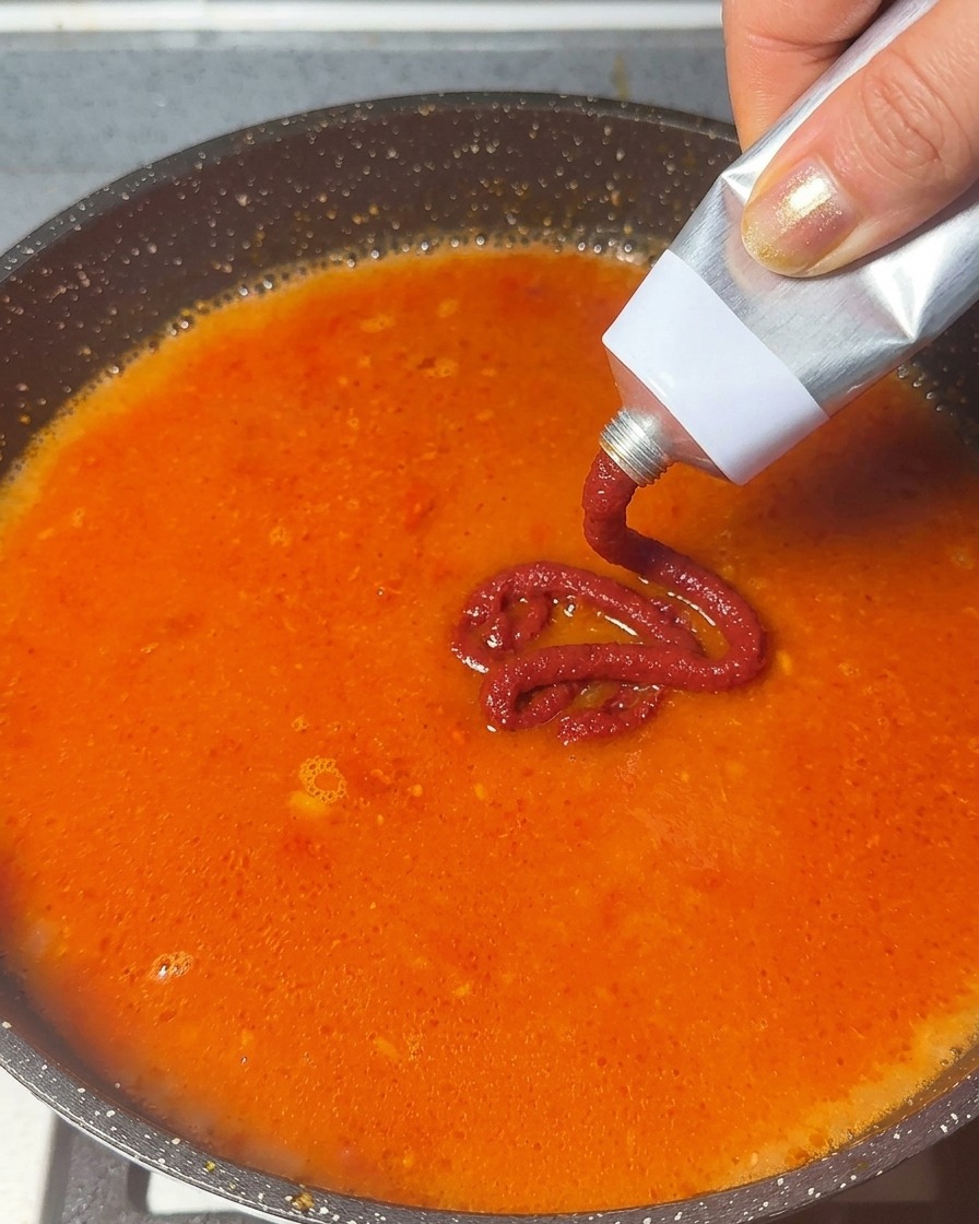 Concentré de tomates pressé depuis un tube dans une base de soupe rouge orangé frémissante.