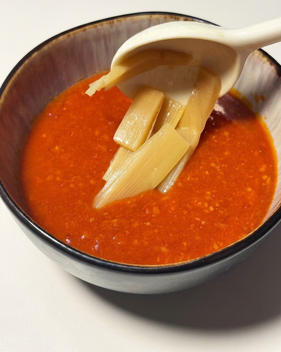 Tranches de pousses de bambou plongées dans un bol de sauce éclatante à la tomate et aux crevettes.