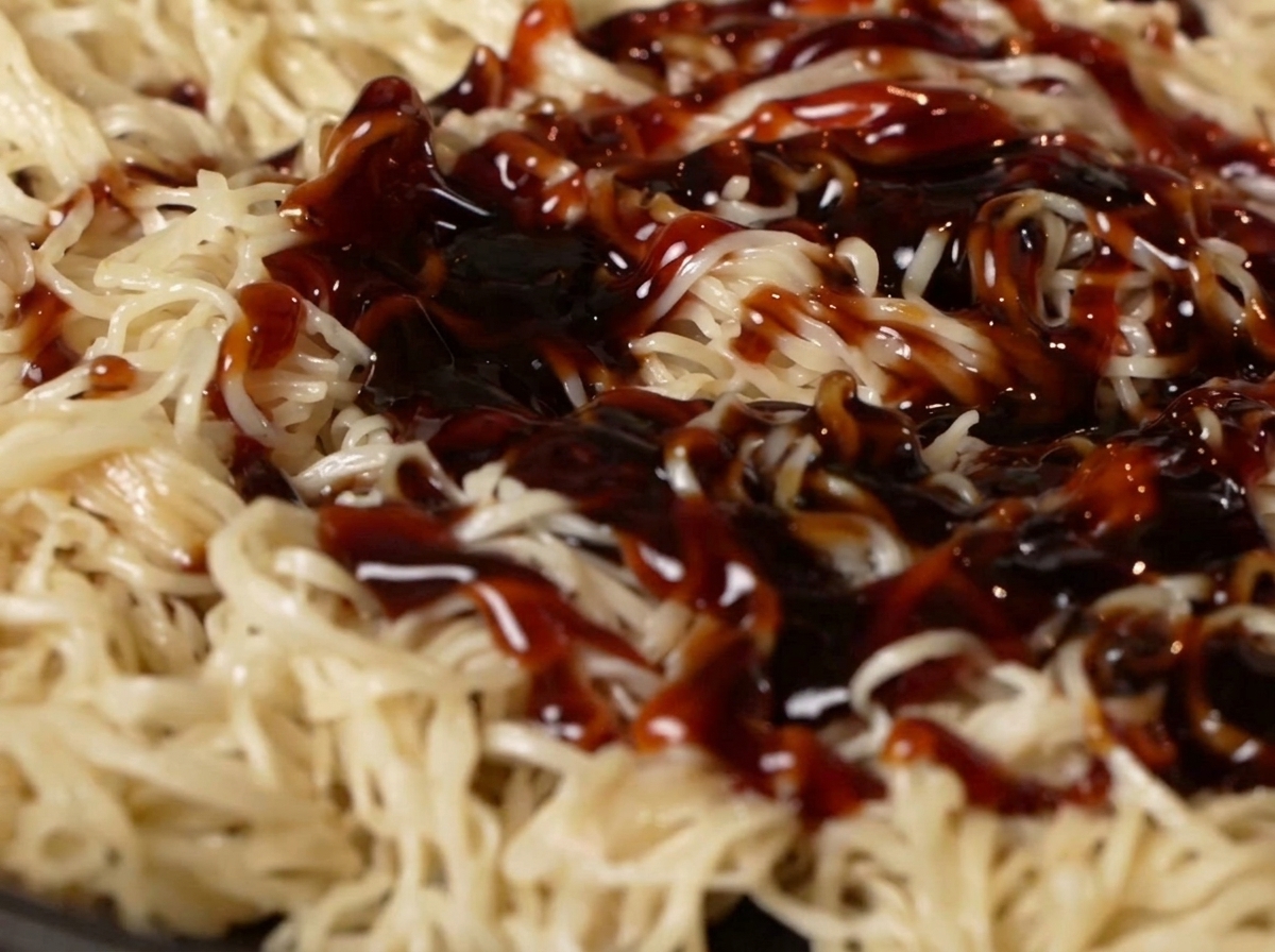 Sauce huître et sauce soja versées sur les nouilles dans la poêle.
