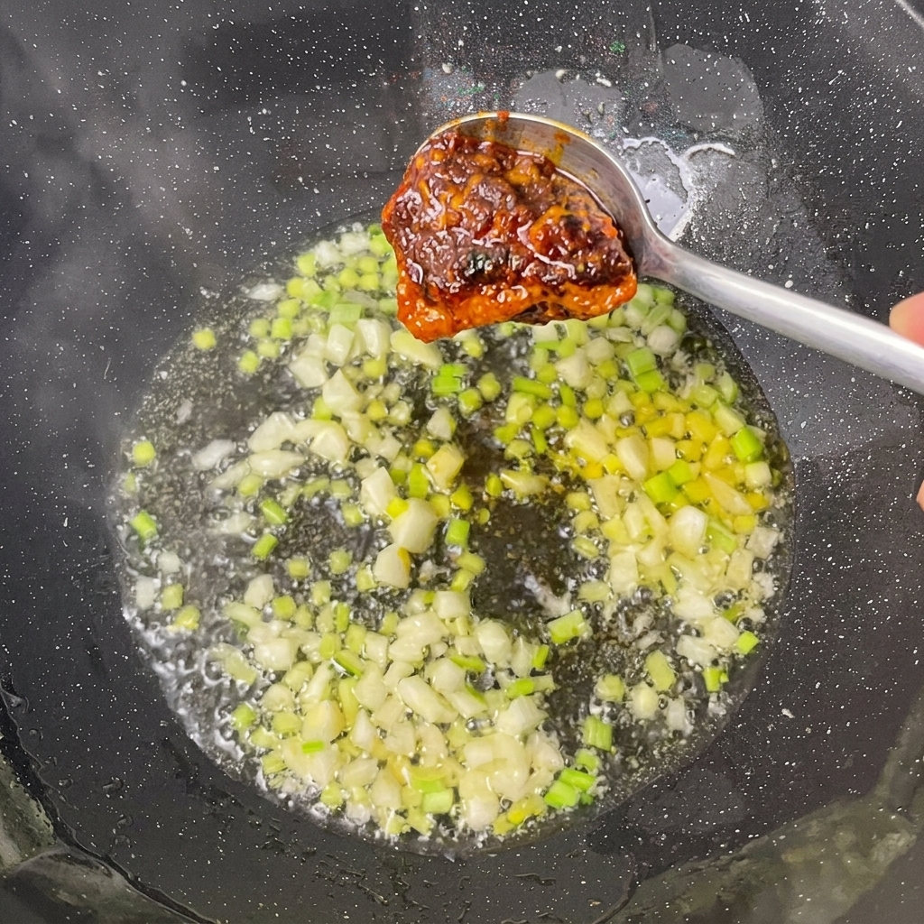 Ajout de la base pour fondue et de la pâte de soja dans le wok avec les aromates.