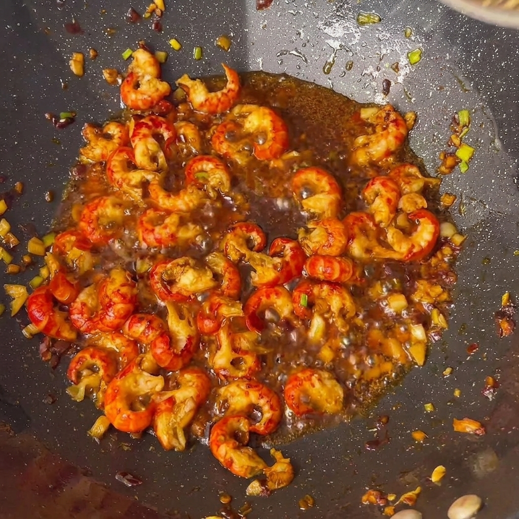 Ajout des sauces et épices sur les queues décrevisses dans le wok.