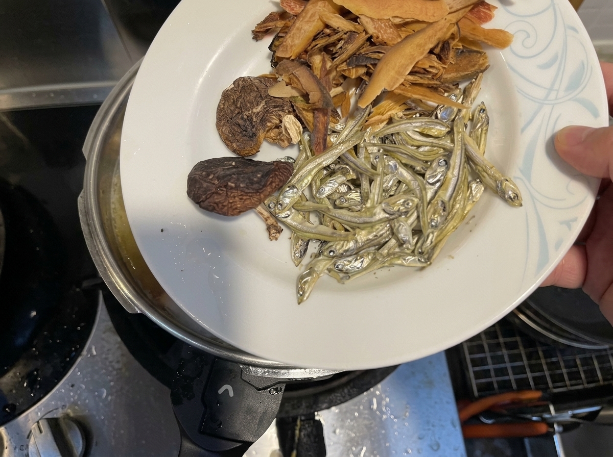 Poissons séchés, champignons shiitake et flocons de poisson ajoutés dans une marmite de liquide frémissant.